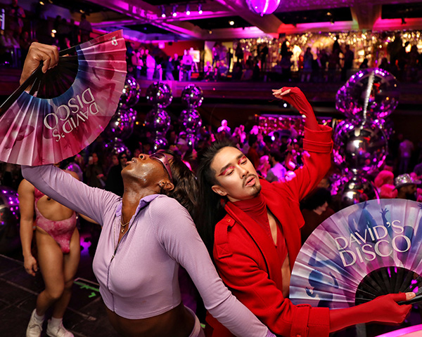 DD_TwoFans Two people posing with David's Disco fans, striking a pose under purply disco lights.