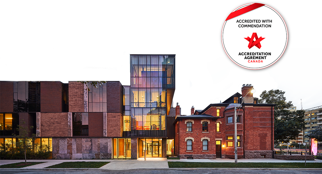 Dec19_Accreditation_Background an image of Casey House with the Accreditation with Commendation Seal in the skyline. The image was taken at dusk so the lights in the front windows cast a warm glow.