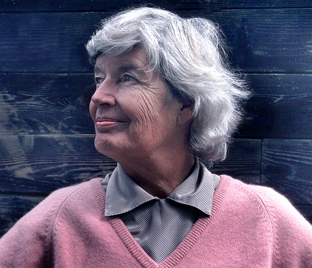 June Callwood Sep 86 -Edit An image of June Callwood wearing a pink wool v neck sweater and a black and white striped shirt underneath that. She has grey hair and her expression is one of pride and confidence.
