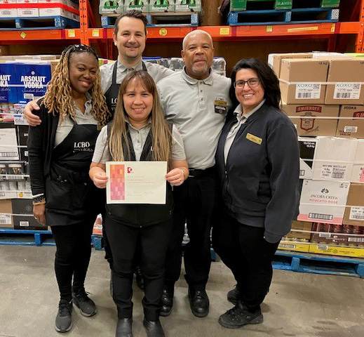 LCBO_Aurelia_Pickering-Edit a group of LCBO warehouse employees posing with a thank you certificate from Casey House for their initiative, "Love Wins"